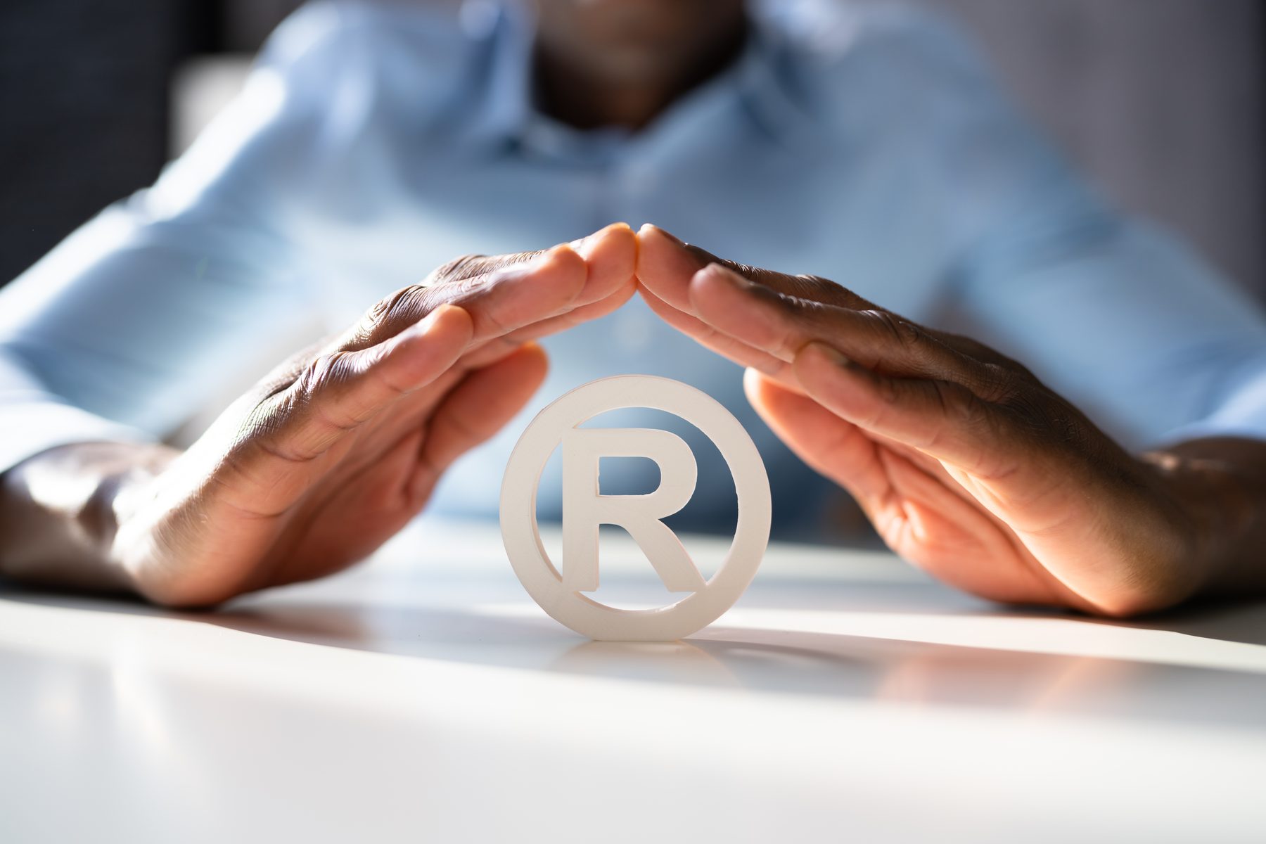 Deborah's hands forming a protective roof over a registered trademark symbol on a white desk